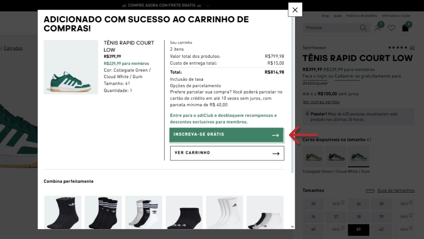 Pop-up de confirmação "ADICIONADO COM SUCESSO AO CARRINHO DE COMPRAS" no site da Adidas, com uma seta apontando para o botão "INSCREVA-SE GRÁTIS".